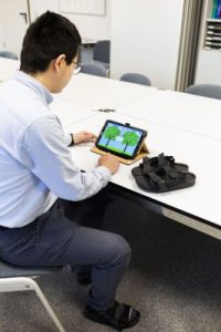 Wissenschaftlicher Mitarbeiter Antao Ming demonstriert die Funktionsweise der Schuhe mit speziellen Einlegesohlen in Verbindung mit dem Spiel auf einem Tablet. Foto: Sarah Kossmann / Universitätsmedizin Magdeburg
