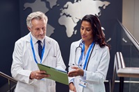 Two Medical Staff Wearing White Coats Discussing Patient Notes Have Informal Meeting In Hospital