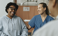 Smiling female nurse consoling happy patient sitting with doctor during consultation at hospital