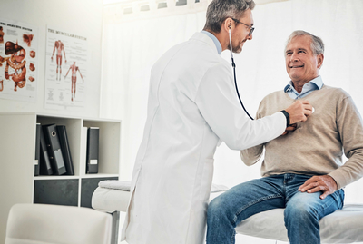 Consultation, man and doctor in checkup with stethoscope, help and advice for healthcare in office. Clinic, senior patient and medical professional at desk with support, trust and heart health on bed