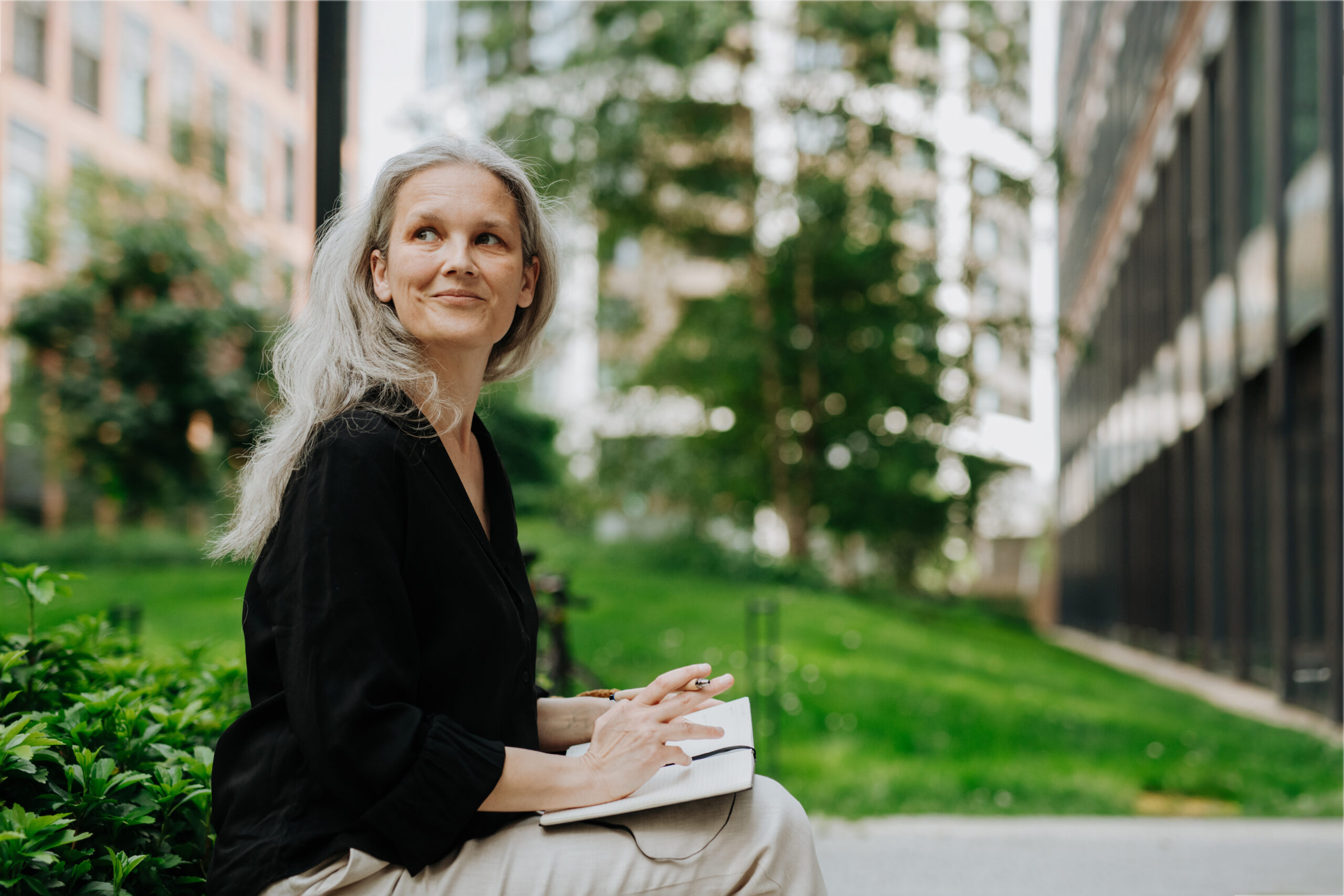 Portrait of beautiful woman with gray hair sitting on bench in city and writing in the notebook.