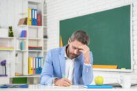 tired school tutor in classroom at blackboard.