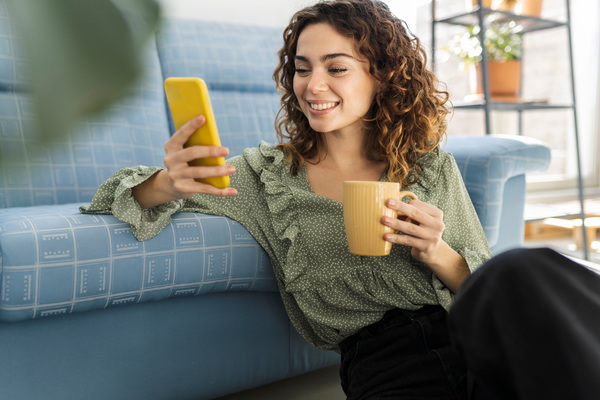 Curly,Haired,Woman,Sitting,On,Sofa,With,A,Cup,Of