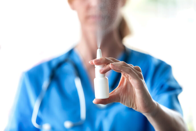 Nahaufnahme einer Ärztin mit einem Nasenspray in der Hand vor weißem Hintergrund.