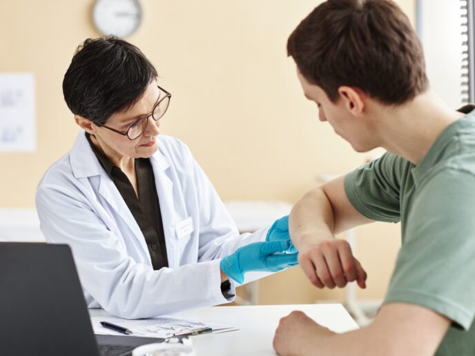 Ärztin untersucht Haut eines Patienten mit Psoriasis