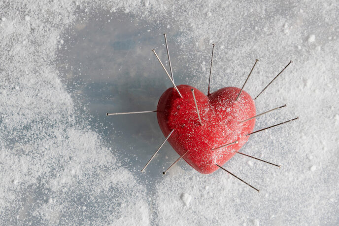 Symbolbild eines mit Nadeln gespickten Herzens auf einem Untergrund aus Zucker.
