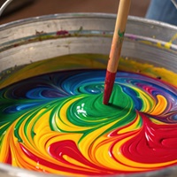A medium closeup of a paint mixing station with vibrant pigments swirling together in a large bucket highlighting the preparation phase of the coating process.