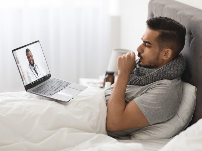 Patient liegt krank im Bett und nutzt eine Online-Sprechstunde.
