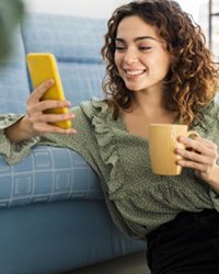 Curly,Haired,Woman,Sitting,On,Sofa,With,A,Cup,Of
